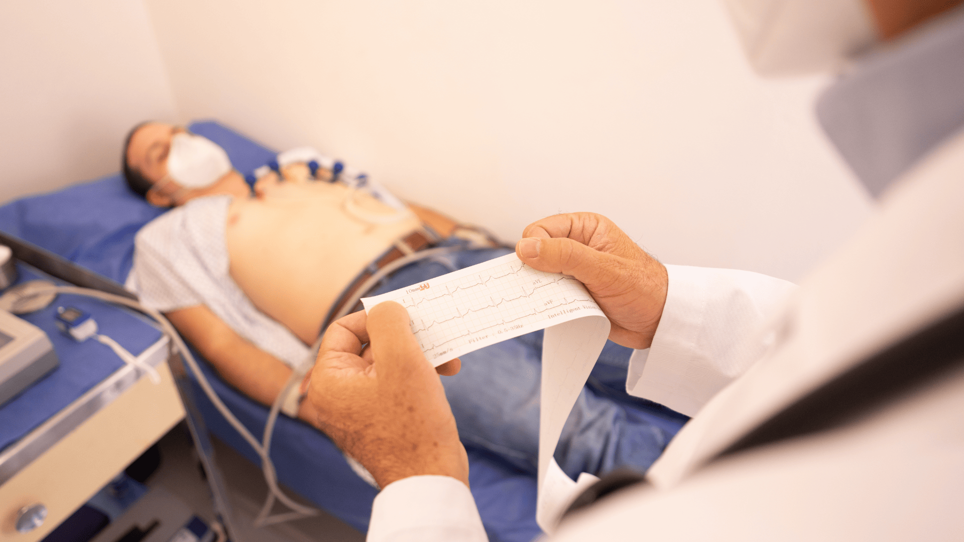 Cardiologo che legge un tracciato elettrocardiografico accanto al paziente disteso con gli elettrodi applicati al torace